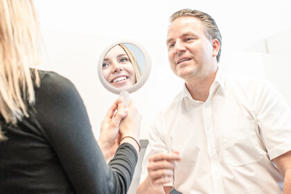 Zahnarzt im Beratungsgespräch mit Patientin und Spiegel zur Darstellung moderner Oralchirurgie in der Zahnarztpraxis Dr. Tolk in Kreuzau